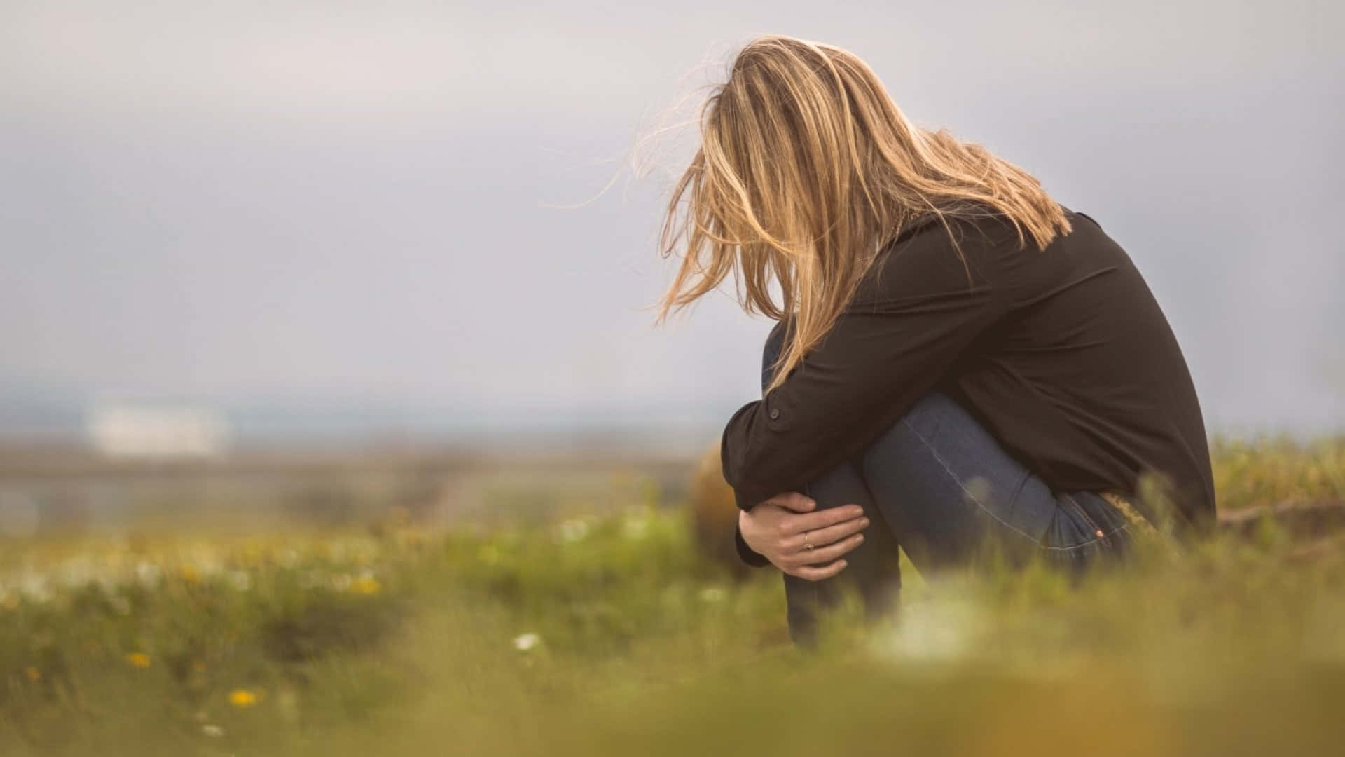 Depressed 桌布 壁紙 — 一位金髮女性蜷縮在草地上，低著頭，雙臂環抱膝蓋，傳達出無聲的悲傷。