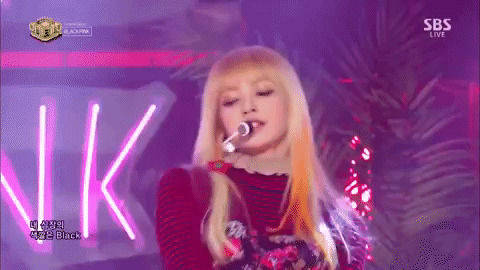 金髮K-pop歌手在紫色霓虹燈下現場表演，背景有棕櫚葉。