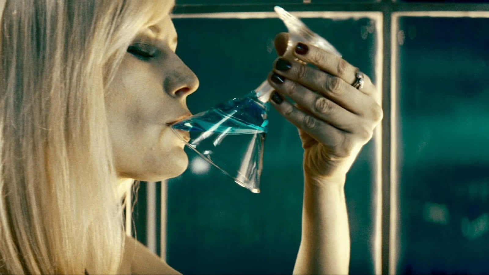 Upside Down 桌布 壁紙 — 一位金髮女郎在燈光昏暗、牆壁呈青綠色的房間裡，從馬丁尼杯中啜飲藍色液體。