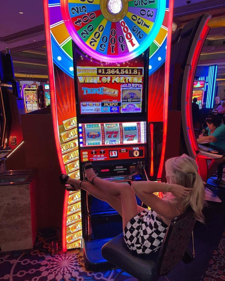 Woman 桌布 壁紙 — 一位金髮女郎在賭場內，悠閒地坐在燈光明亮的 Wheel of Fortune 老虎機前。