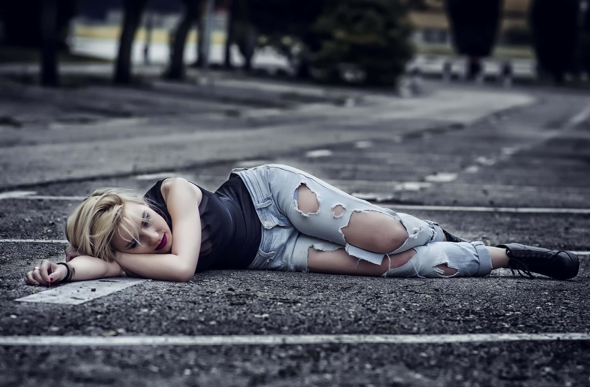 女孩 桌布 壁紙 — 一位金髮年輕女子側臥在鋪砌的道路上，穿著破洞牛仔褲和黑色上衣。
