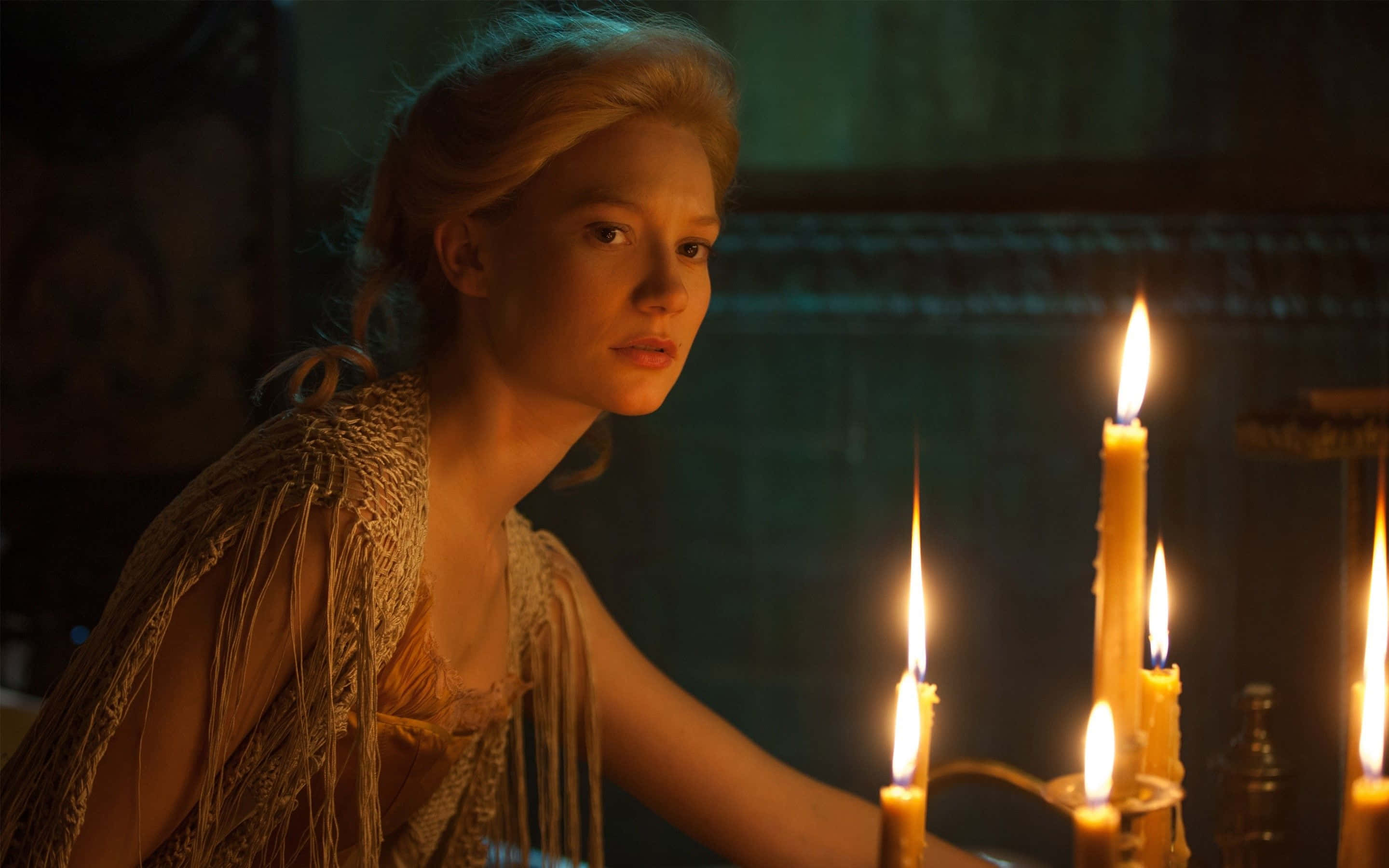 Mia Wasikowska 桌布 壁紙 — 一位金髮年輕女子在昏暗的房間裡，在搖曳的燭光旁若有所思地凝視著。