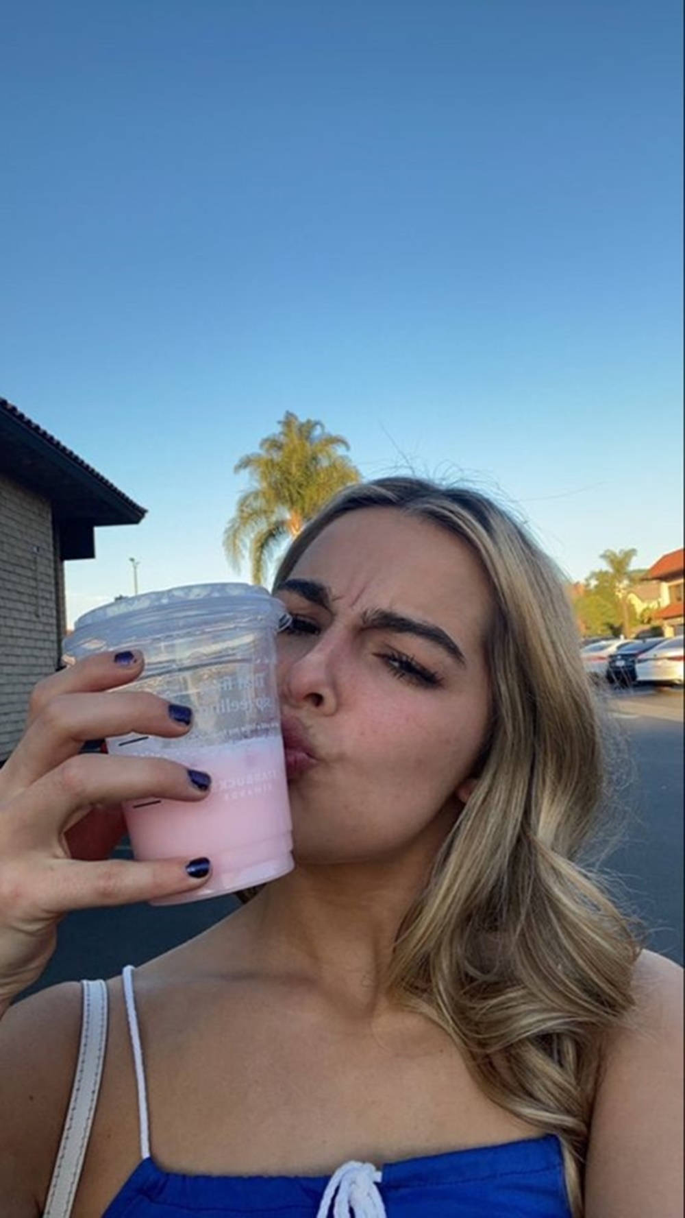 Cute Girl 桌布 壁紙 — 一位金髮年輕女性在晴朗藍天下，於戶外從杯子中啜飲粉紅色飲料。
