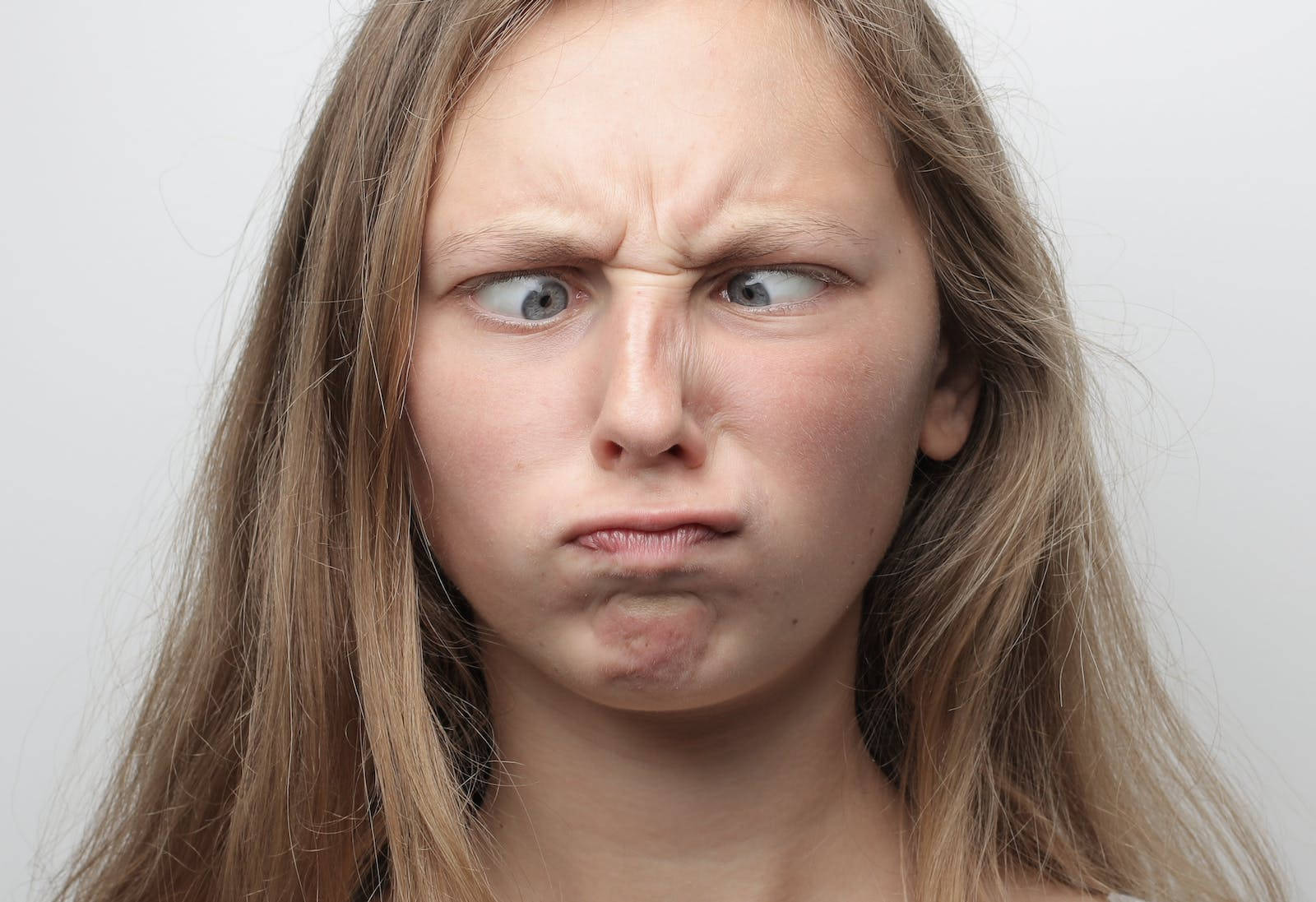 搞笑 桌布 壁紙 — 一位金髮年輕女性在純白背景前，瞇起眼睛、皺起鼻子，做出兇狠憤怒的表情。