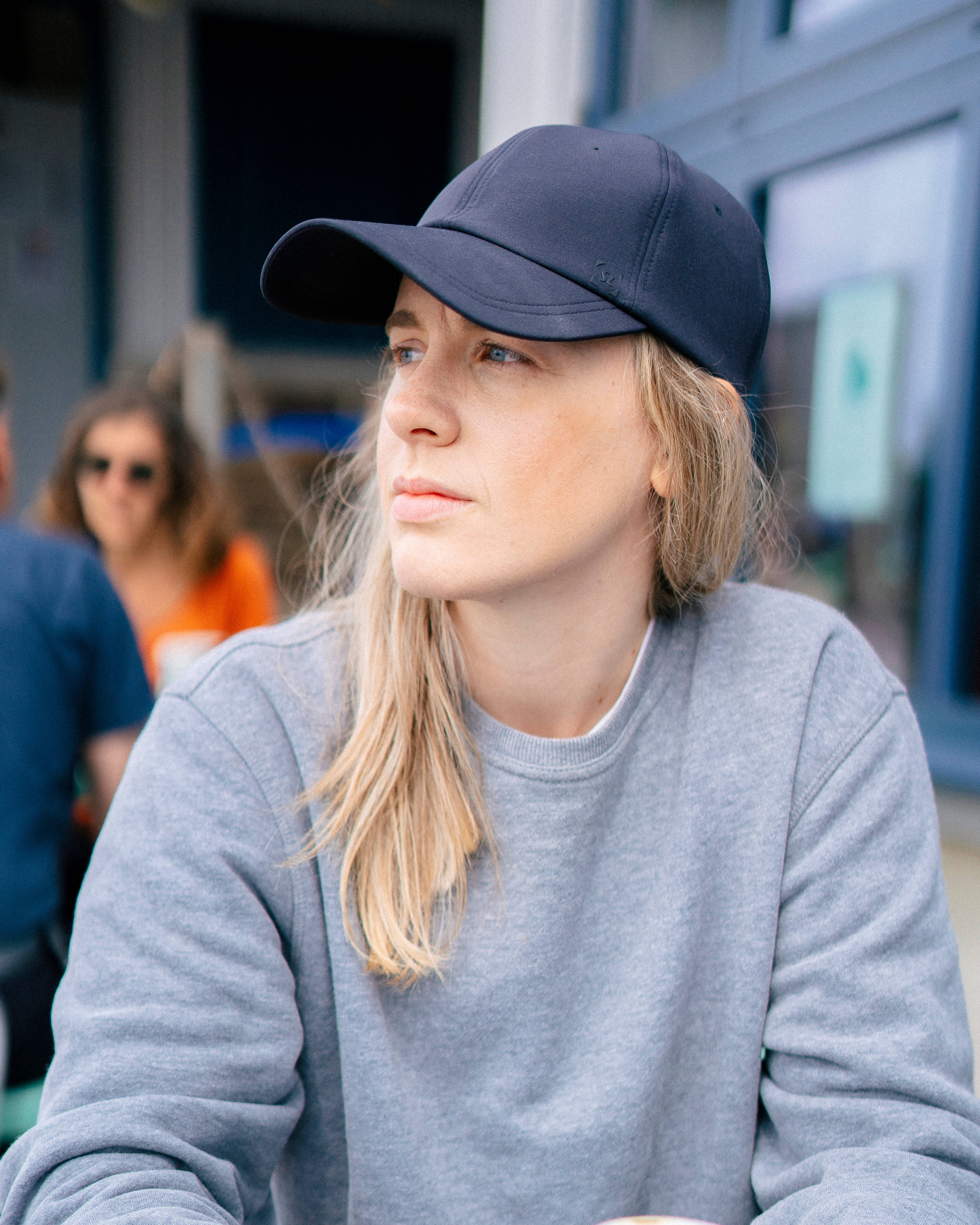 Tomboy 桌布 壁紙 — 一位金髮年輕女性戴著深色帽子及灰色衛衣，若有所思地望向戶外。