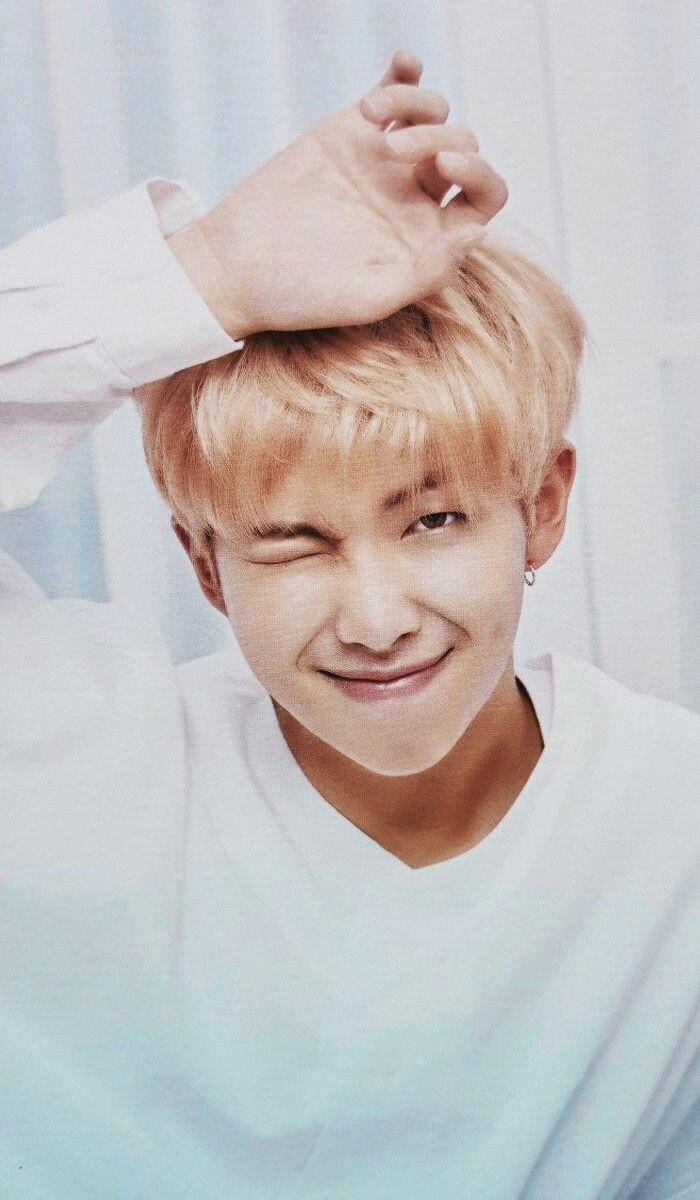 BTS 桌布 壁紙 — 一位金髮年輕男子在柔軟的藍色窗簾背景下，將手放在頭上俏皮地眨眼。