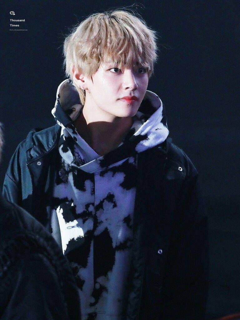Taehyung Cute 桌布 壁紙 — 一位金髮年輕男子在深色背景前穿著黑色外套，內搭黑白紮染連帽衫。