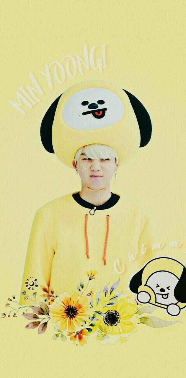 Cute Bts 桌布 壁紙 — 一位金髮年輕男子戴著黃色狗主題帽子和連帽衫，背景是淺黃色，飾有花卉圖案和卡通角色。