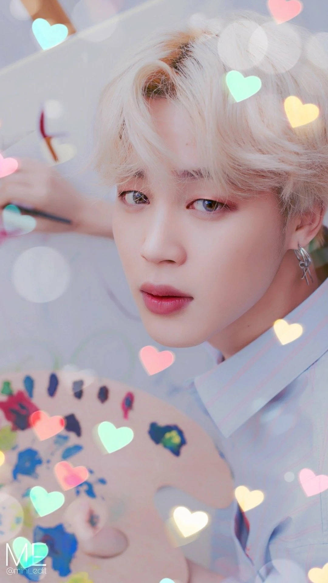 Jimin Bts Cute 桌布 壁紙 — 一位金髮年輕男子手持調色板，溫柔地凝視著，發光的愛心在夢幻的粉彩薄霧中漂浮在他周圍。