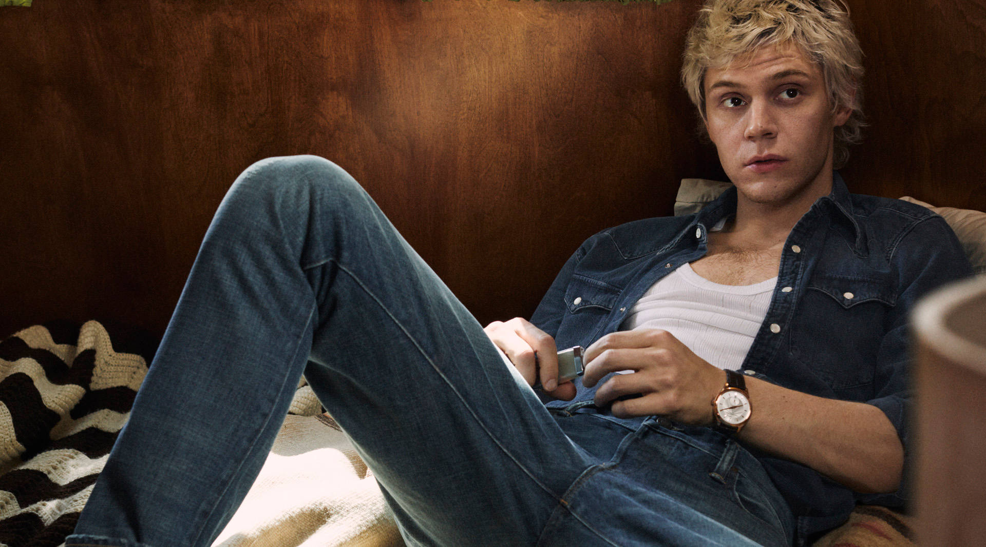 Tate Langdon 桌布 壁紙 — 一位金髮年輕男子穿著牛仔褲和牛仔襯衫，隨意地躺在床上，手持電話。