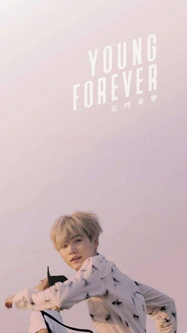 Suga Bts 桌布 壁紙 — 一位金髮年輕男子穿著鳥圖案襯衫，在柔和的粉紅色天空下擺姿勢，帶有「YOUNG FOREVER」文字。
