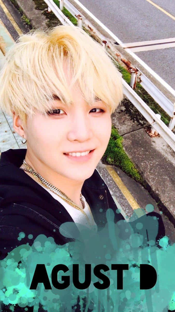 Agust D 桌布 壁紙 — 一位金髮年輕男子站在路邊，帶有青綠色潑濺圖形覆蓋層，對著鏡頭微笑。
