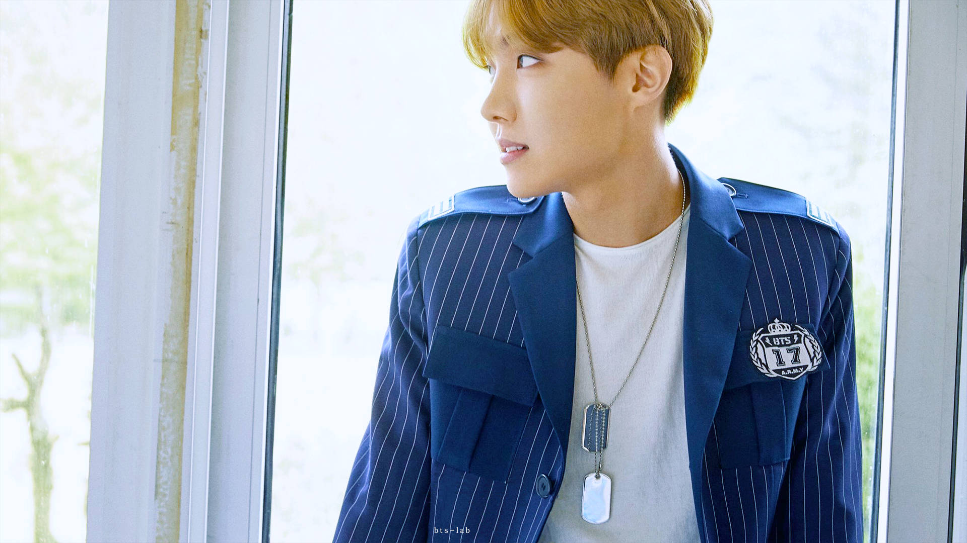 BTS 桌布 壁紙 — 一位金髮年輕男子身穿海軍藍細條紋西裝外套，若有所思地望著明亮的窗外。