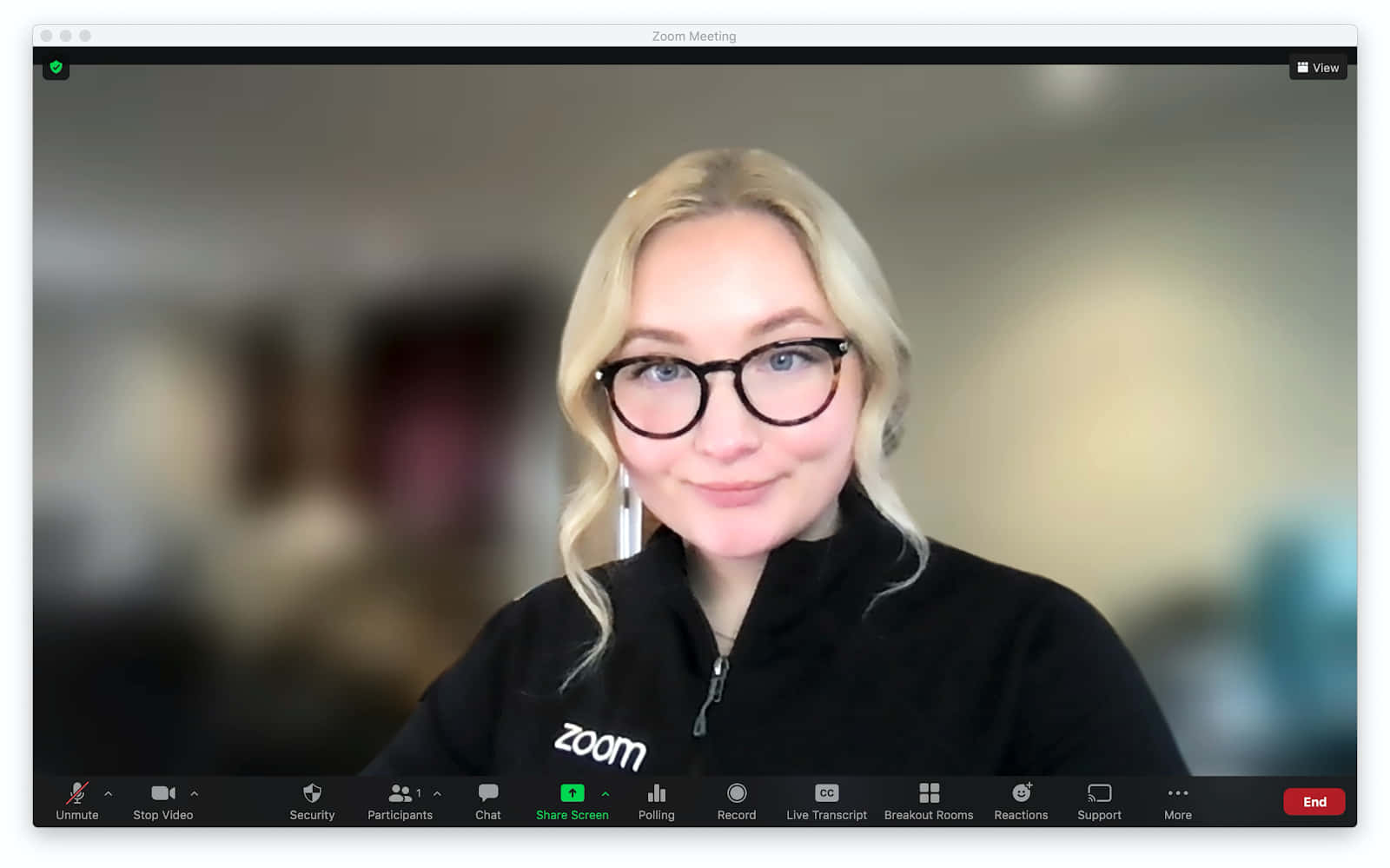 Blurry 桌布 壁紙 — 一位金髮戴眼鏡的女性在Zoom視訊通話中微笑，身穿帶有Zoom標誌的黑色拉鍊外套。