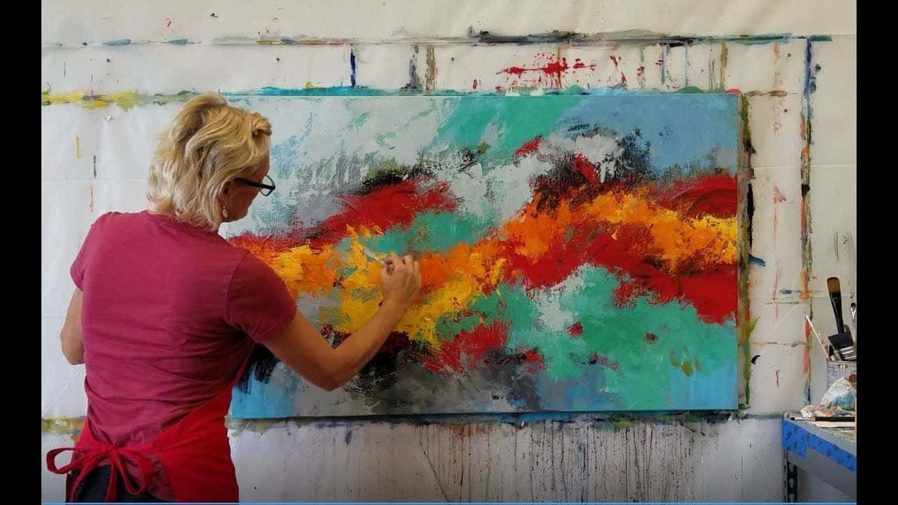 Painting 桌布 壁紙 — 一位金髮戴眼鏡的女性在凌亂的工作室中用大膽的紅色、橙色和青色筆觸繪製大型抽象畫布。