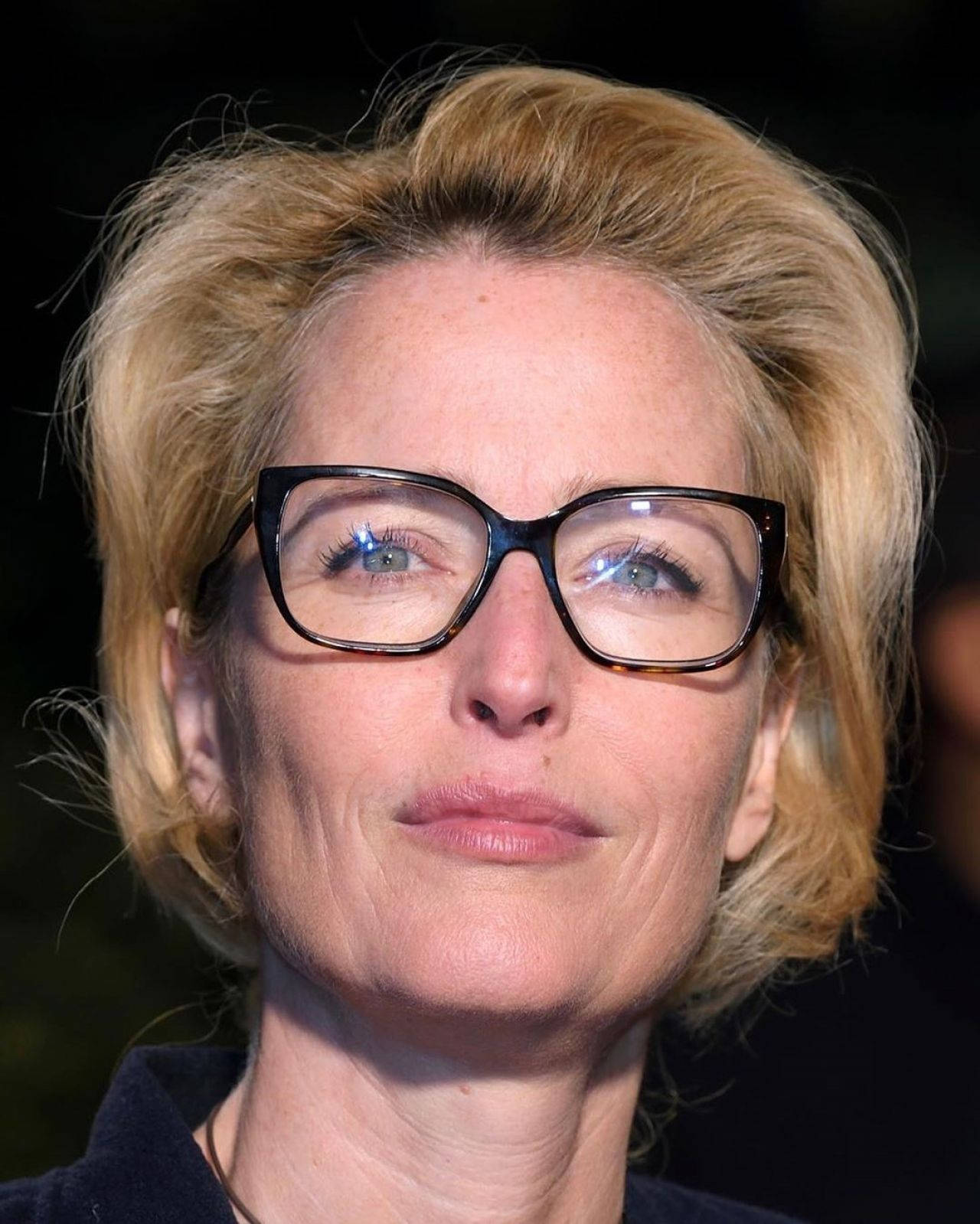 gillian anderson 桌布 壁紙 — 一位金髮戴眼鏡的女性近距離肖像，面無表情地直視鏡頭。