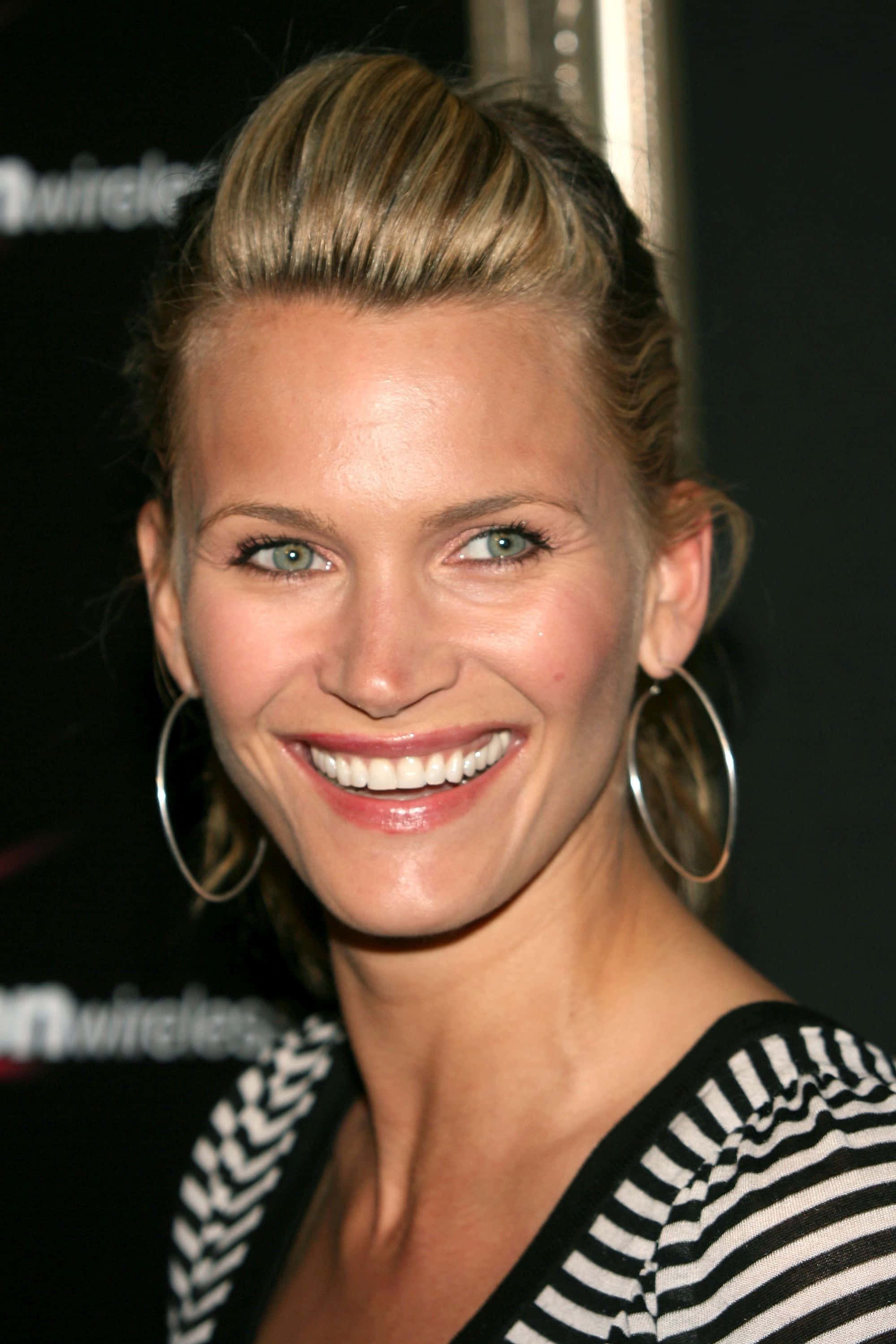 Natasha Henstridge 桌布 壁紙 — 一位金髮戴著圓環耳環的燦爛女性，穿著黑白條紋上衣微笑。