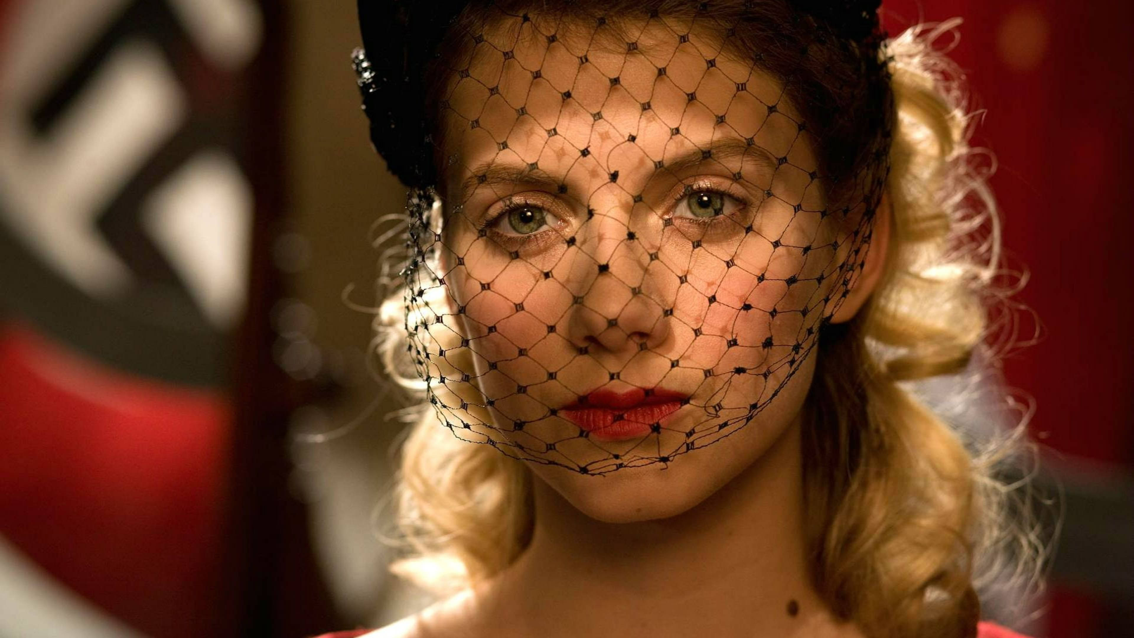 Inglourious Basterds 桌布 壁紙 — 一位金髮捲曲、紅唇的女性戴著黑色網紗面罩，在模糊的納粹旗幟背景下凝視鏡頭。