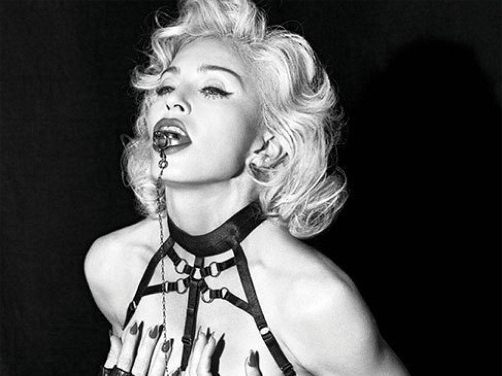 Madonna 桌布 壁紙 — 一位金髮捲曲、身穿皮革束具、嘴裡含著鏈條的女性的黑白肖像。