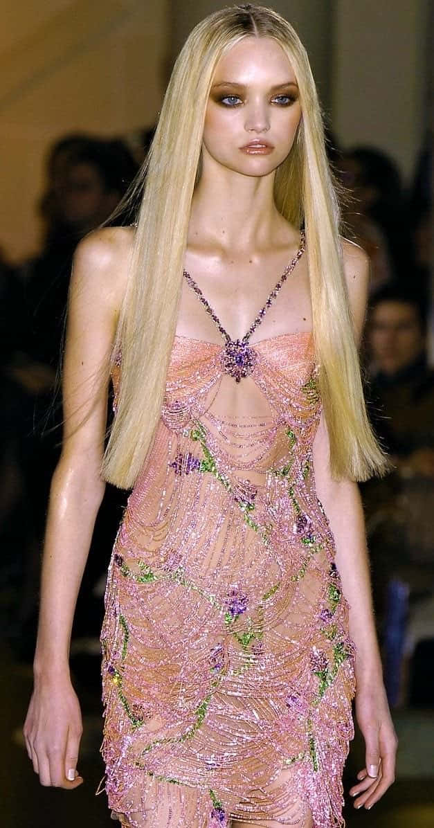 Gemma Ward 桌布 壁紙 — 一位金髮模特兒在溫暖的走秀燈光下，自信地穿著一件閃閃發光的粉紅色珠飾禮服，上面有花卉刺繡。