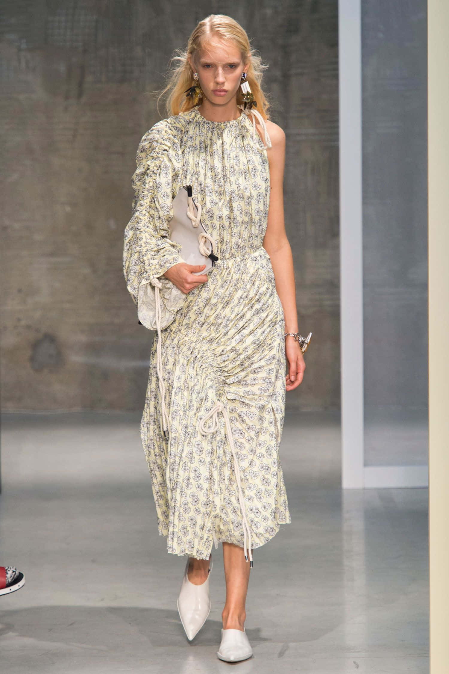 Runway 桌布 壁紙 — 一位金髮模特兒自信地走在伸展台上，身穿印花洋裝，帶有褶皺細節和白色尖頭高跟鞋。
