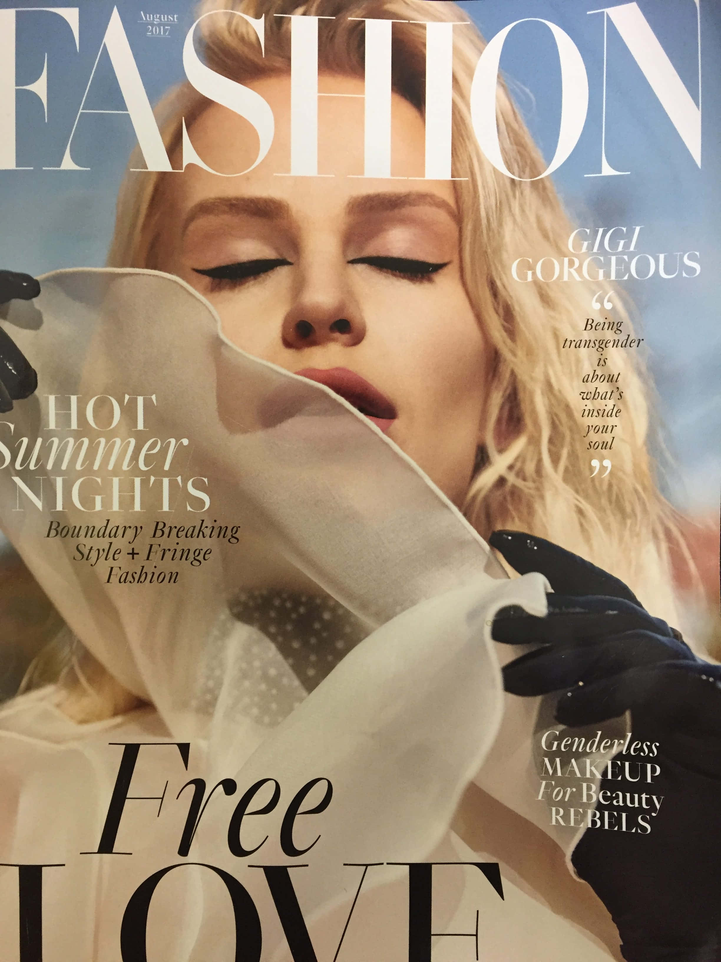 雜誌 桌布 壁紙 — 一位金髮模特兒閉上眼睛，畫著大膽眼線，戴著黑色手套，手持半透明白色布料，背景是明亮的藍天。