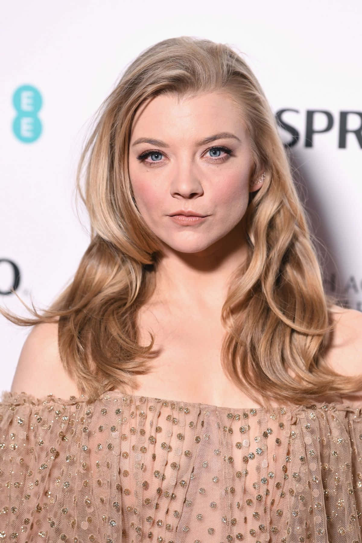 natalie dormer 桌布 壁紙 — 一位金髮波浪長髮、藍眼睛的女性在活動中穿著閃亮露肩連衣裙的特寫肖像。