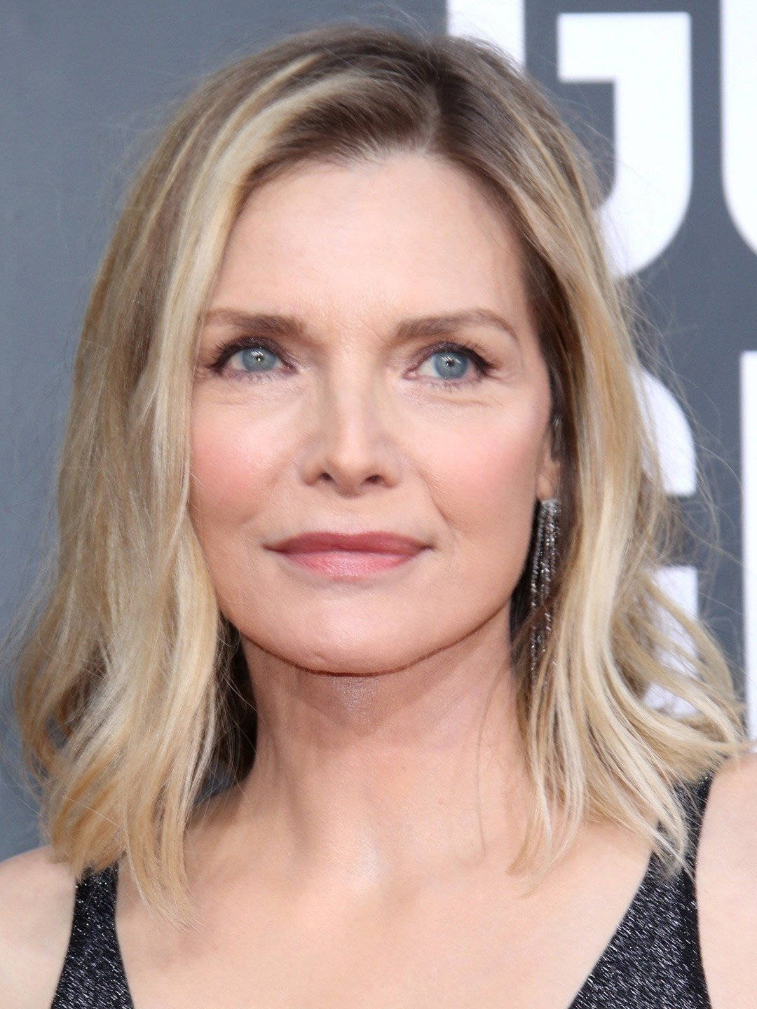 Celebrity 桌布 壁紙 — 一位金髮波浪髮型、藍眼睛的女性特寫肖像，戴著垂墜耳環和黑色上衣。