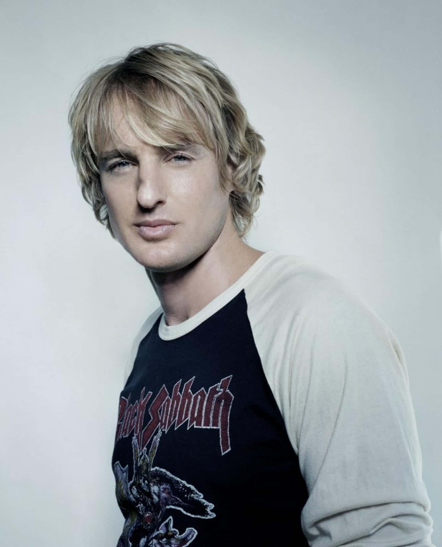 Owen Wilson 桌布 壁紙 — 一位金髮男子穿著一件黑白配色的拉格倫衫，上面有黑色安息日標誌，背景是純淺灰色。