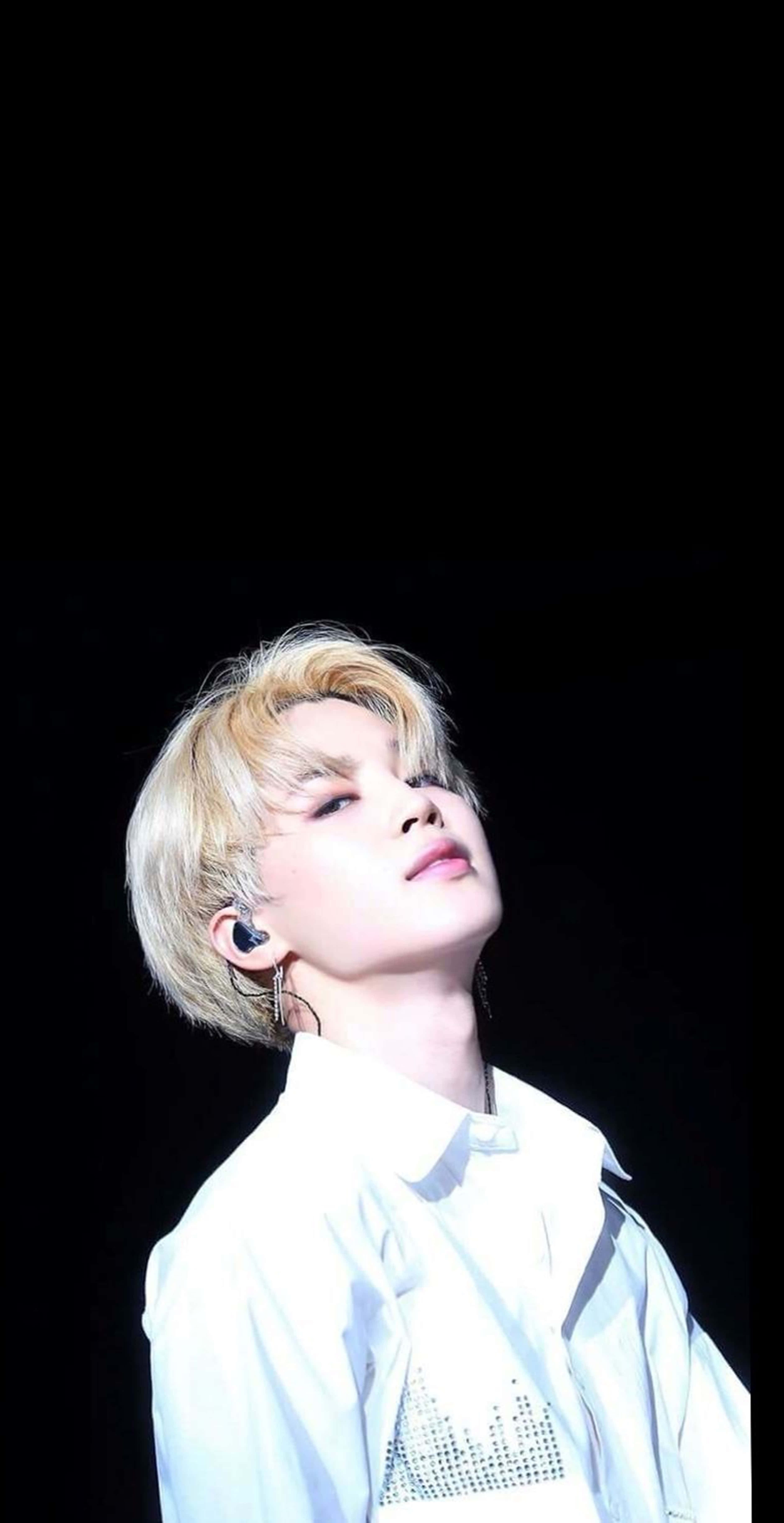 BTS 桌布 壁紙 — 一位金髮白襯衫的年輕男子在黑色背景下，於明亮的舞台燈光中向上凝視。