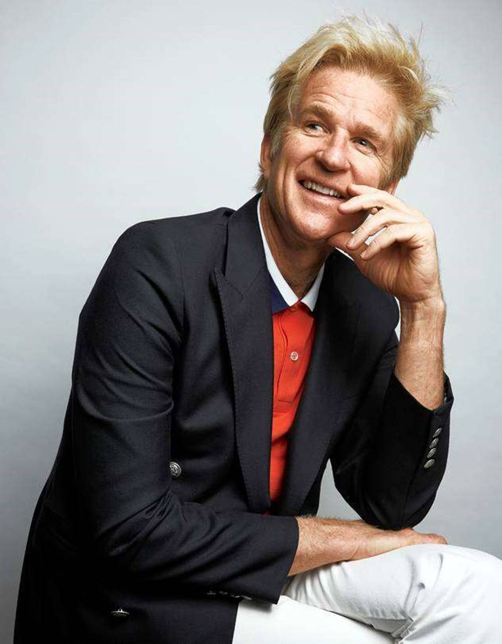Celebrity 桌布 壁紙 — 一位金髮的開朗男子，在純灰色背景上，將下巴擱在手上，溫暖地微笑。