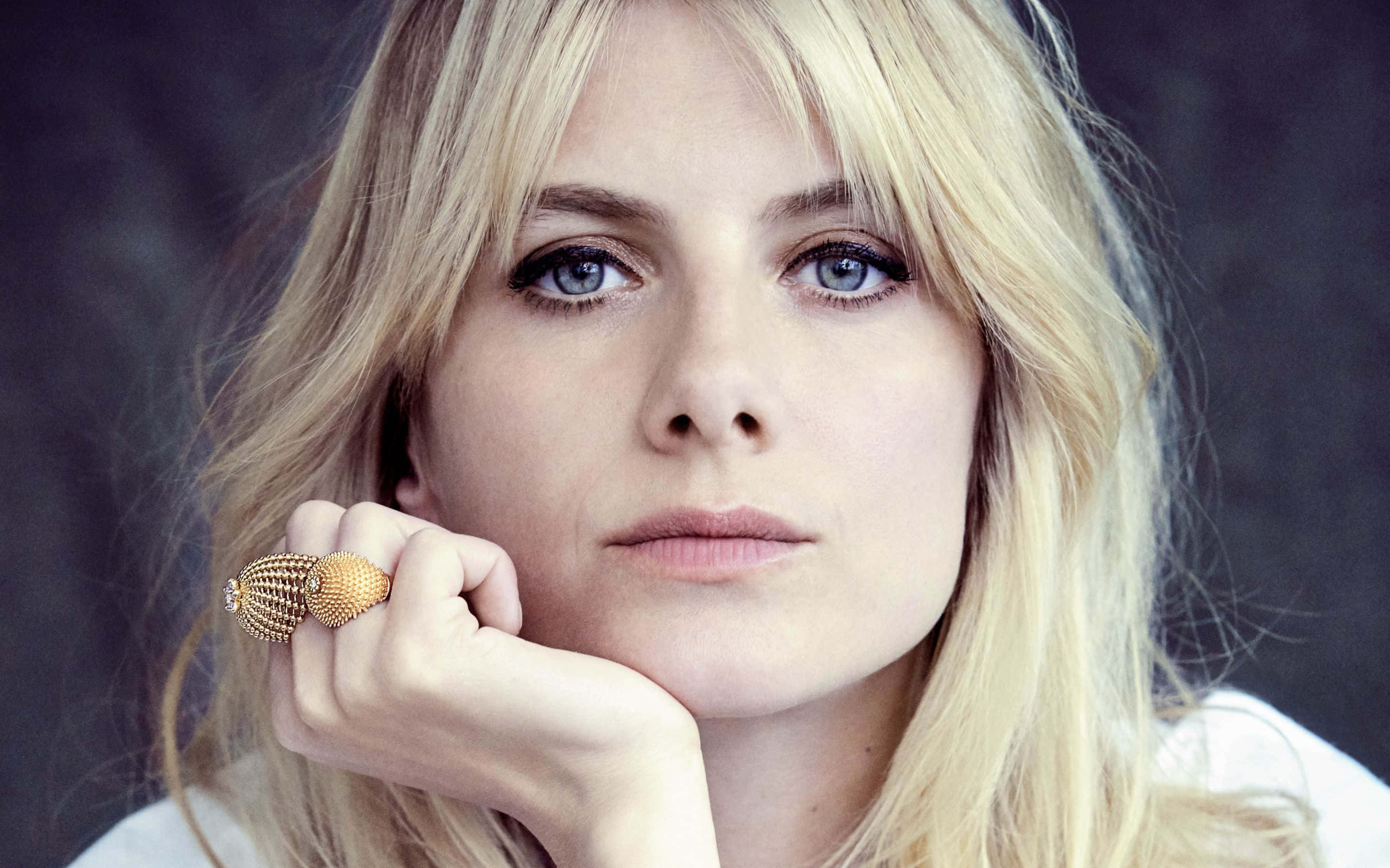 Mélanie Laurent 桌布 壁紙 — 一位金髮碧眼、令人驚豔的女性特寫肖像，她將下巴擱在戴著金戒指的手上。