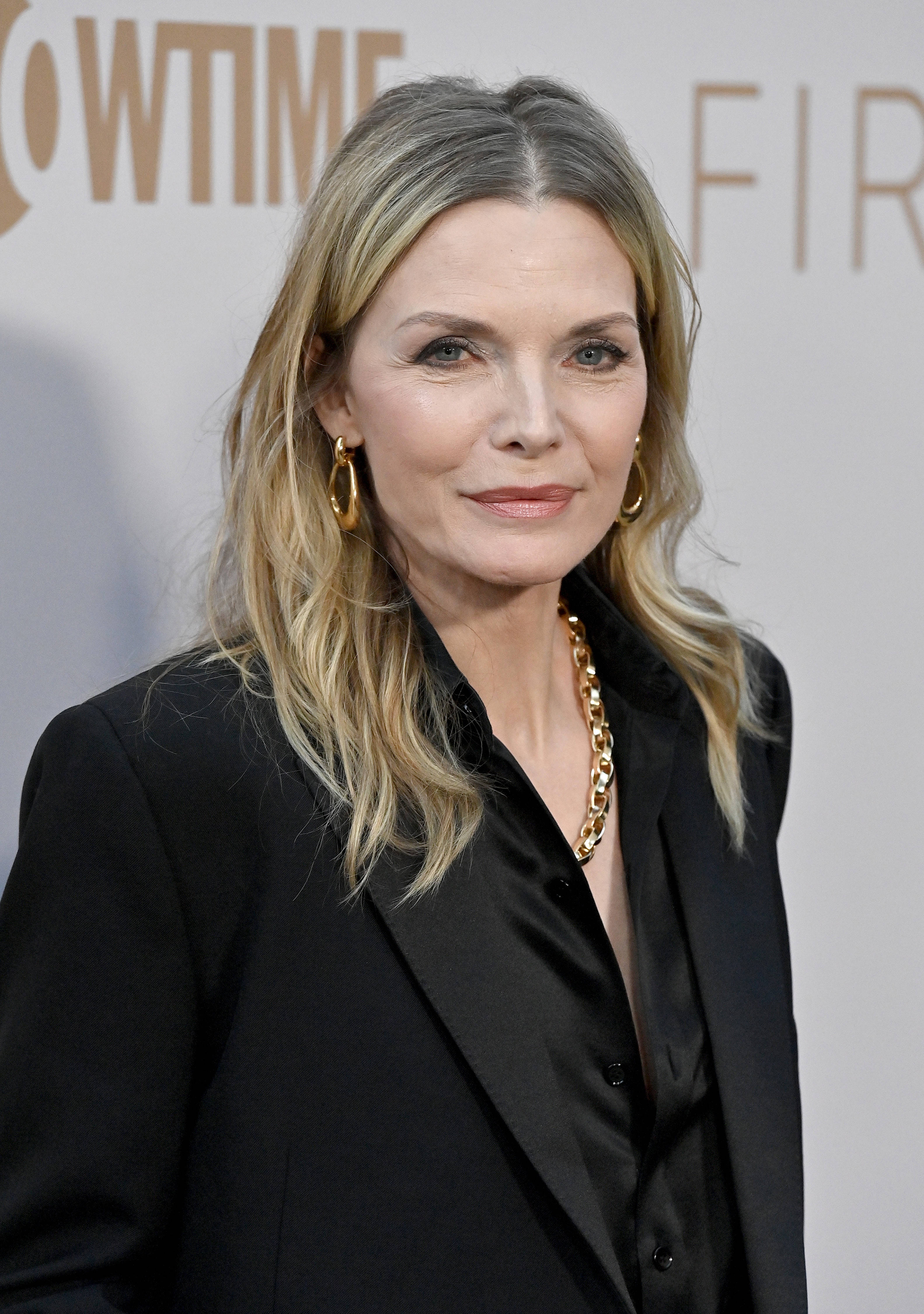 Hollywood 桌布 壁紙 — 一位金髮碧眼、佩戴金飾的優雅女士，在正式場合穿著黑色西裝外套。
