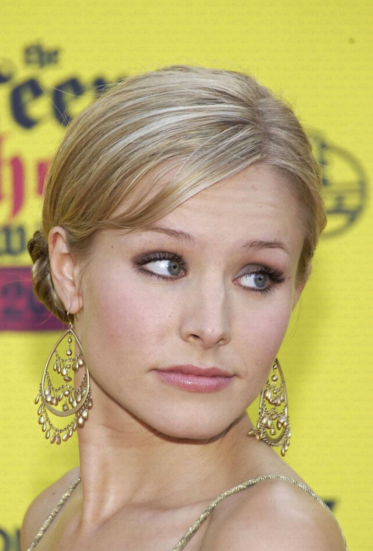 kristen bell 桌布 壁紙 — 一位金髮碧眼、戴著華麗金耳環的女性，在明亮的黃色背景下拍攝的特寫肖像。