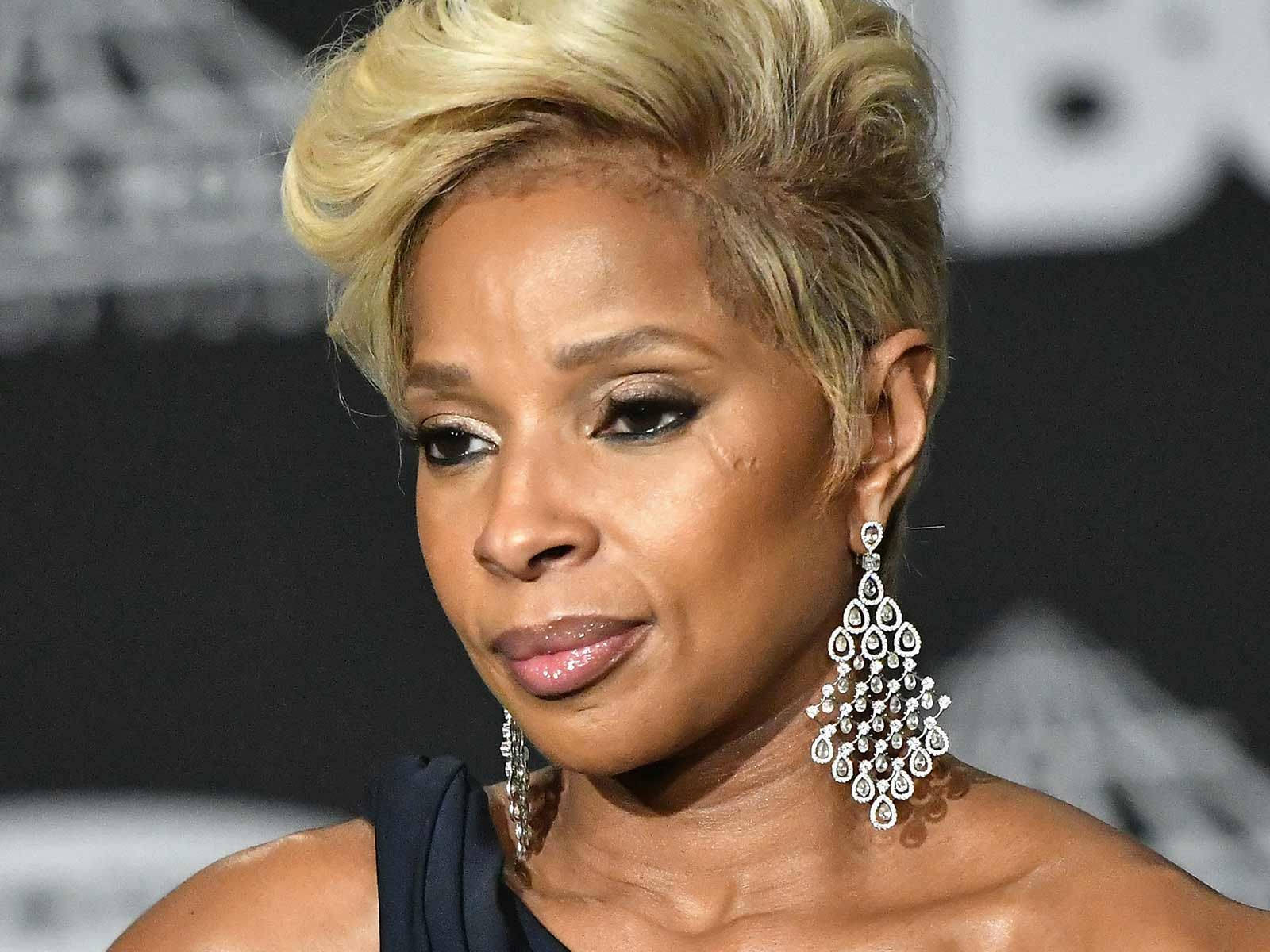 Celebrity 桌布 壁紙 — 一位金髮碧眼、戴著閃爍吊燈耳環的迷人女性，自信地穿著深色連衣裙擺姿勢。