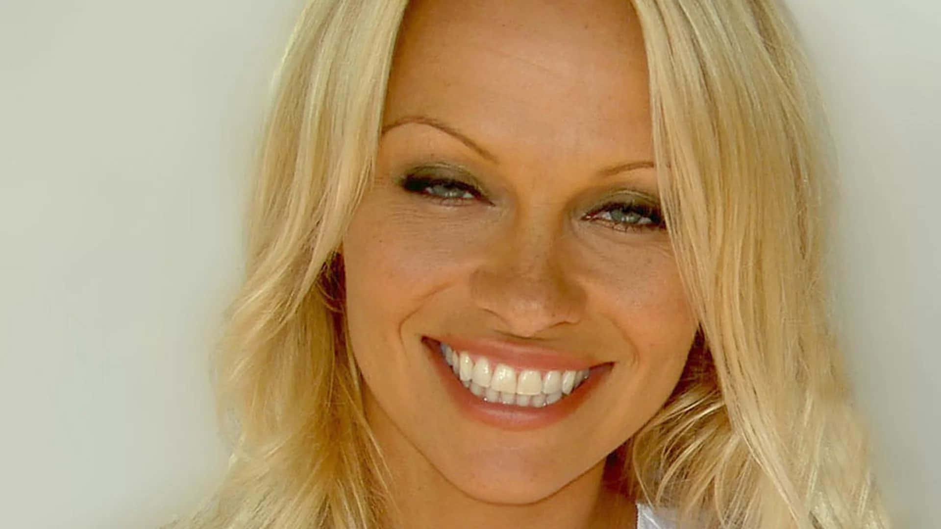 pamela anderson 桌布 壁紙 — 一位金髮碧眼、擁有明亮綠色眼睛的女性，在純白背景前溫暖微笑的特寫肖像。