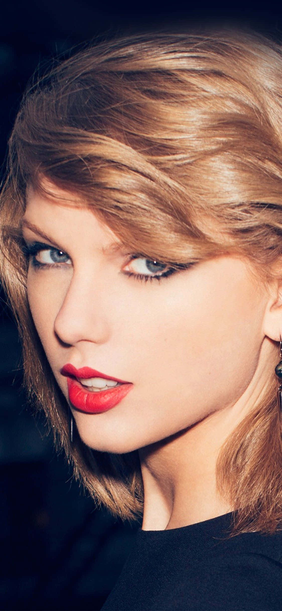 Taylor Swift iPhone 桌布 壁紙 — 一位金髮碧眼、擁有鮮豔紅唇的女性直視鏡頭的近距離肖像。