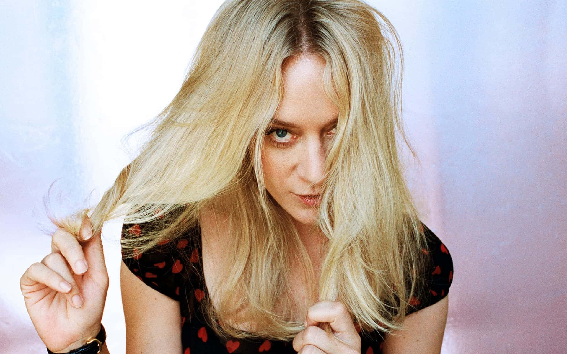 Chloë Sevigny 桌布 壁紙 — 一位金髮碧眼、眼神深邃的女性，一邊俏皮地握著自己飄逸的髮絲，一邊直視鏡頭。