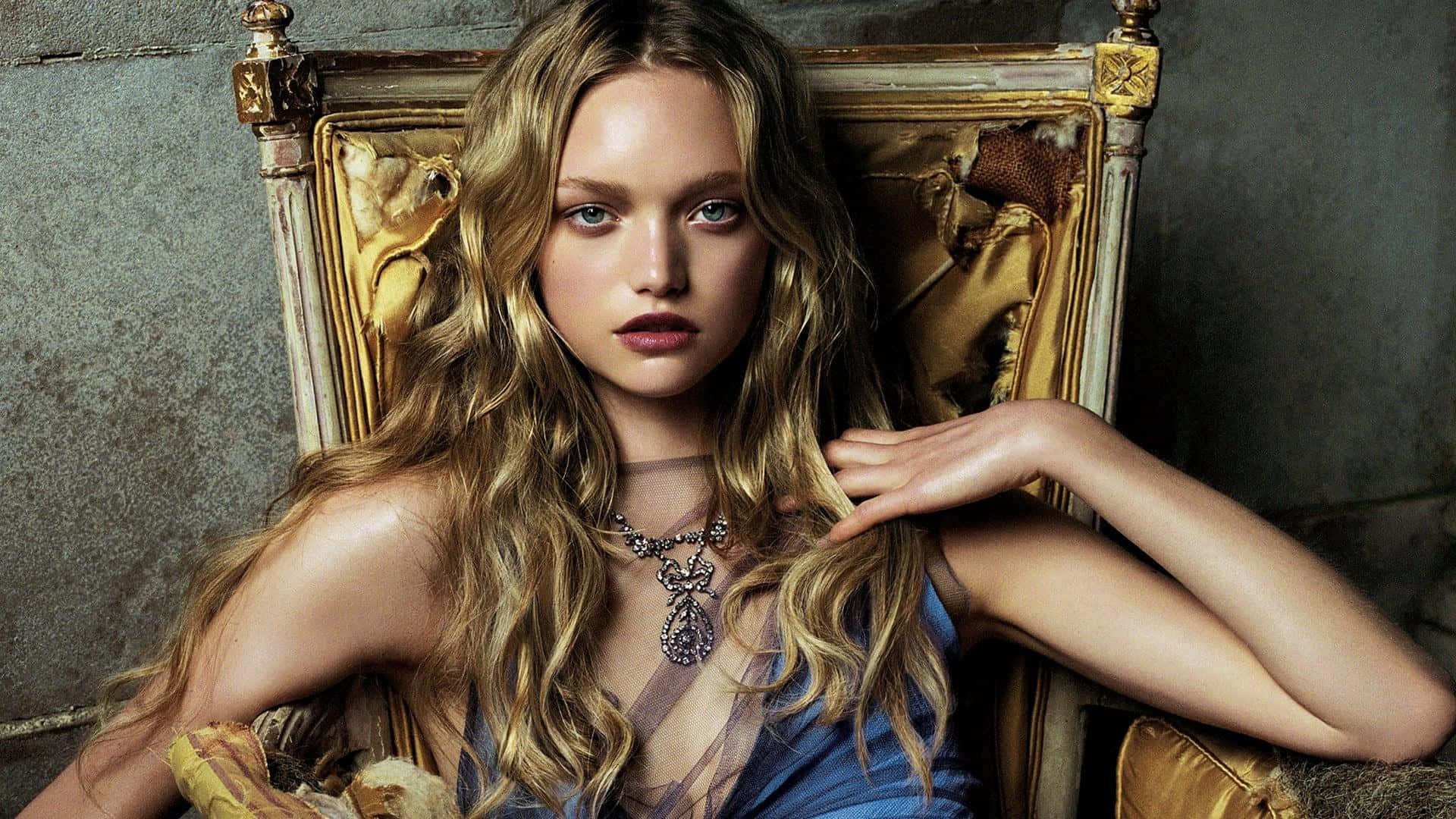 Gemma Ward 桌布 壁紙 — 一位金髮碧眼、眼神銳利的女子，端坐在磨損的金色王座上，背景是紋理灰牆。