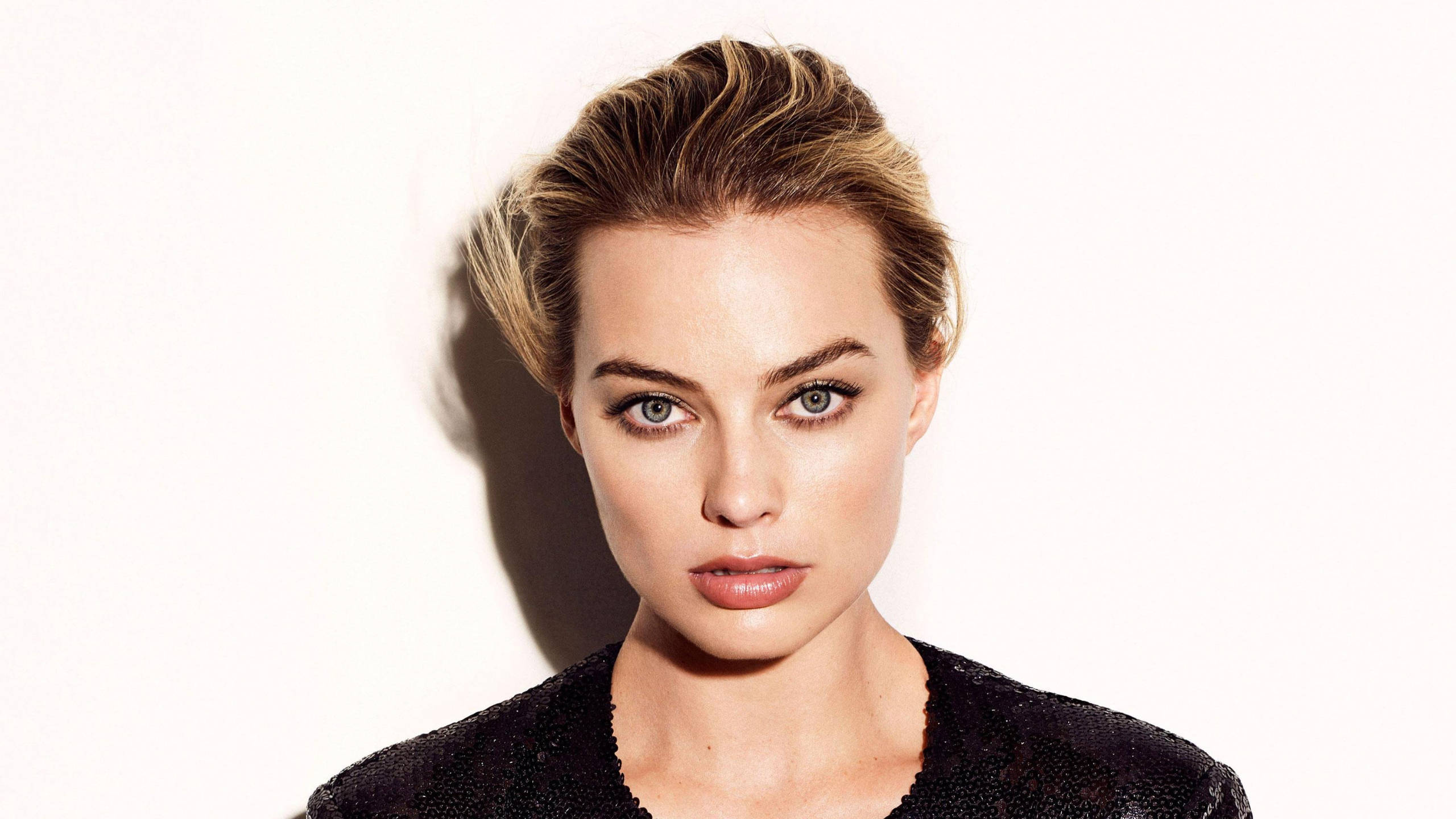Margot Robbie 桌布 壁紙 — 一位金髮碧眼、眼神銳利的女性，在純白背景下的引人注目的肖像。