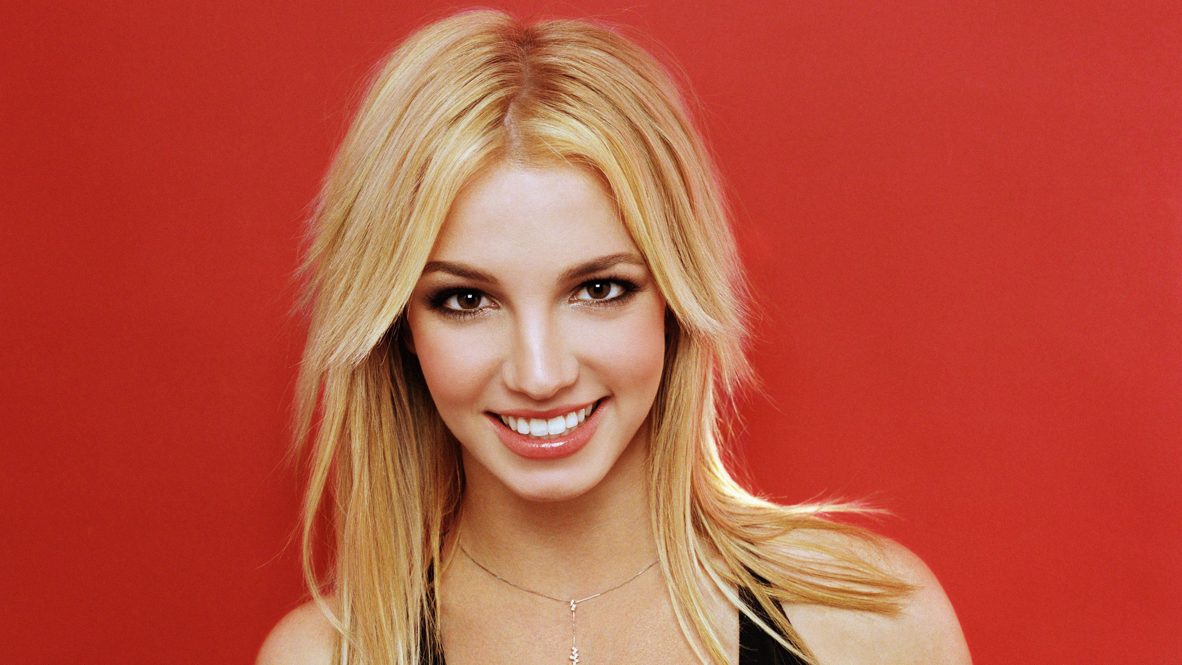 britney 桌布 壁紙 — 一位金髮碧眼、笑容燦爛的女性站在大膽的紅色背景前。