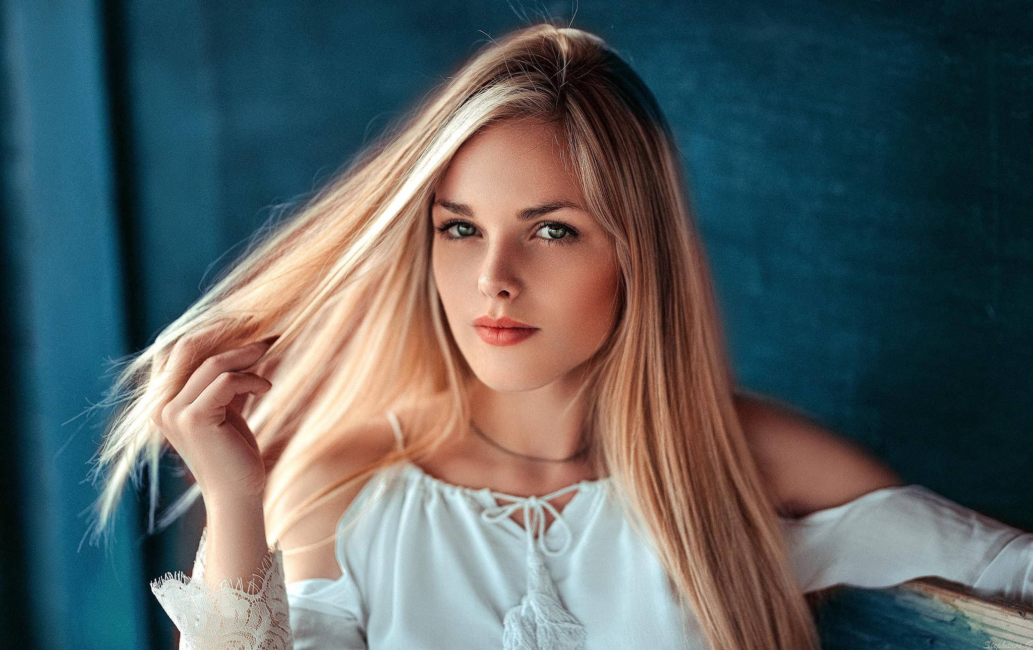 Blonde Woman 桌布 壁紙 — 一位金髮碧眼（綠色眼睛）的女性在深藍色紋理背景上輕柔地觸摸她的頭髮。