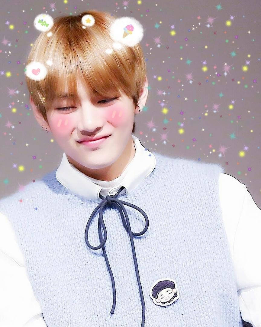 Taehyung Cute 桌布 壁紙 — 一位金髮碧眼、臉頰紅潤的年輕男子，身穿淺藍色針織背心內搭白色襯衫，在閃爍的粉彩背景前溫柔微笑。