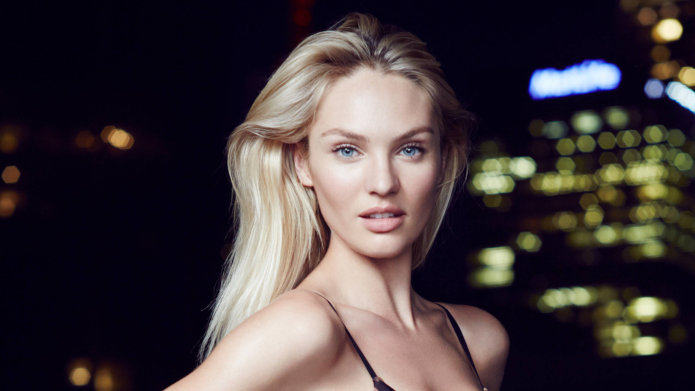 Candice 桌布 壁紙 — 一位金髮碧眼的女性在模糊的夜間城市燈光背景下凝視前方。