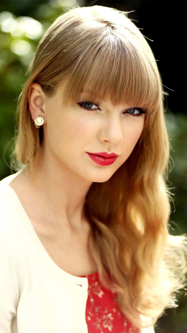 Taylor Swift iPhone 桌布 壁紙 — 一位金髮紅唇的女性在模糊的綠色背景下微笑的特寫肖像。