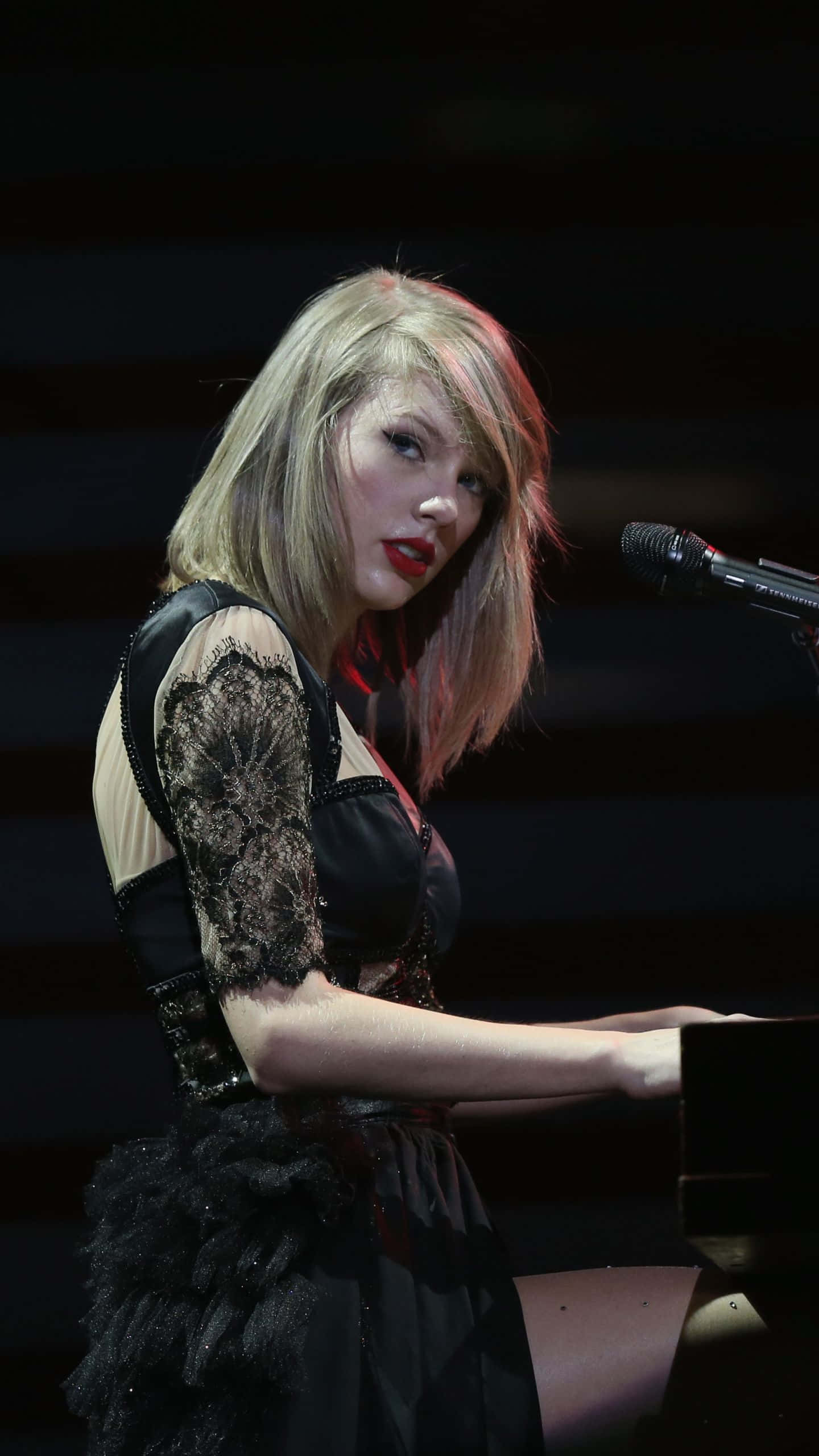 Singer 桌布 壁紙 — 一位金髮紅唇的女性在舞台燈光下彈鋼琴，旁邊有麥克風。