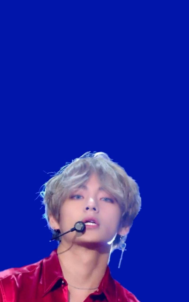 Kim Taehyung 2021 桌布 壁紙 — 一位金髮紅衫的年輕男子在純藍色背景前對著麥克風唱歌。