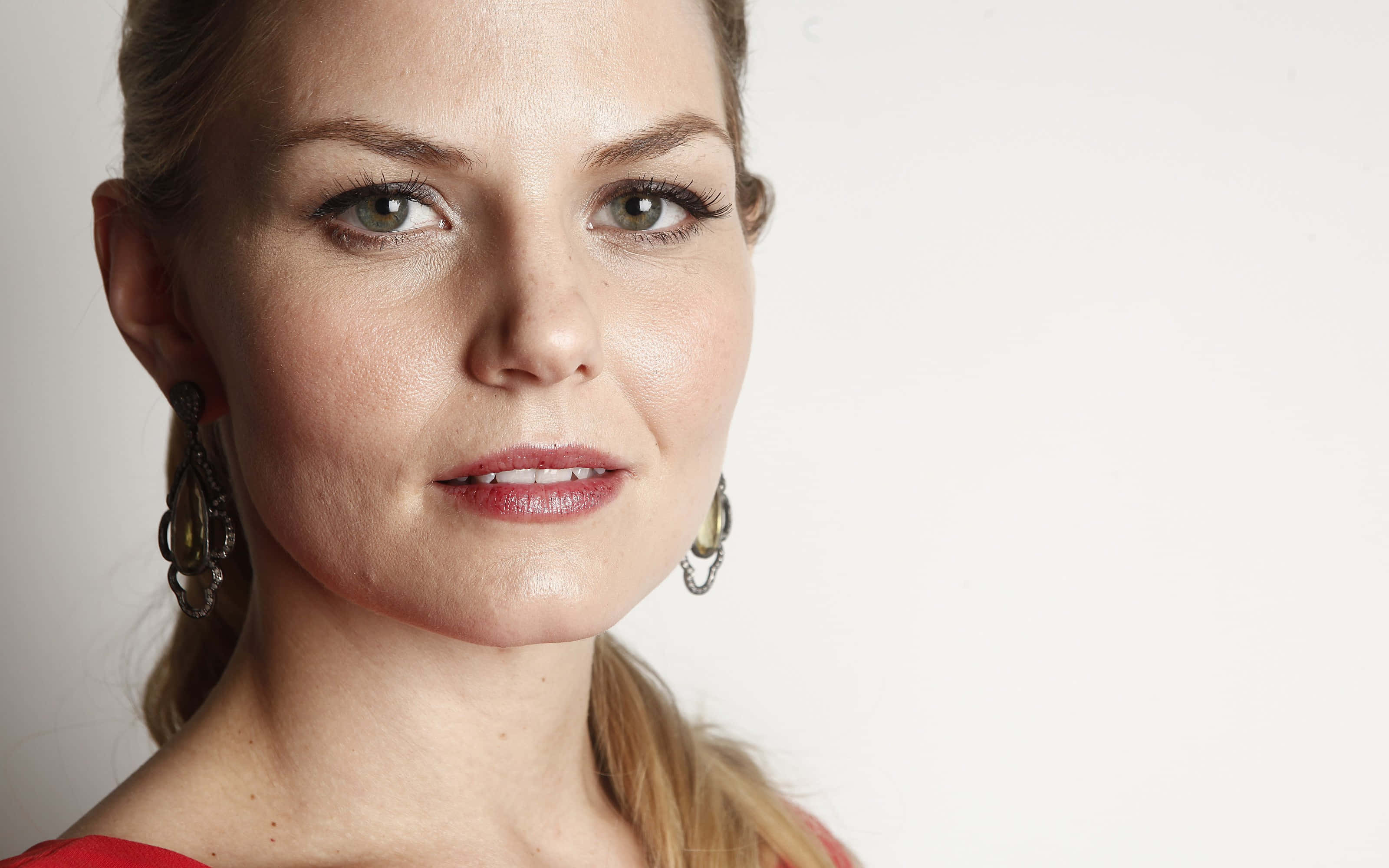 jennifer morrison 桌布 壁紙 — 一位金髮綠眼女性穿著紅色上衣和垂墜耳環，在純白背景前的特寫肖像。