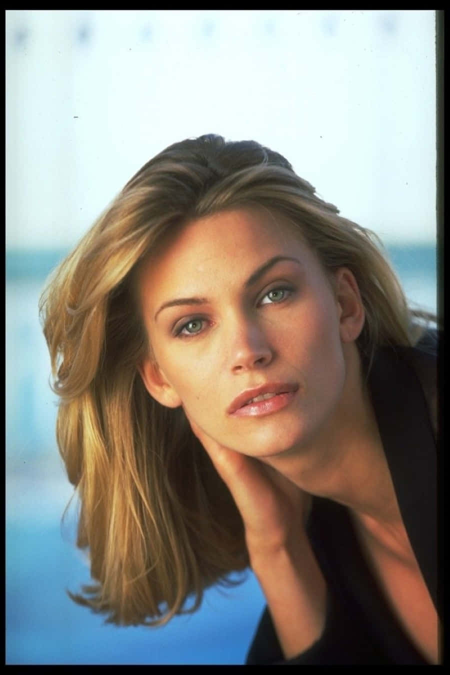 Natasha Henstridge 桌布 壁紙 — 一位金髮綠眼的女性，在模糊的藍色背景前，托腮沉思。