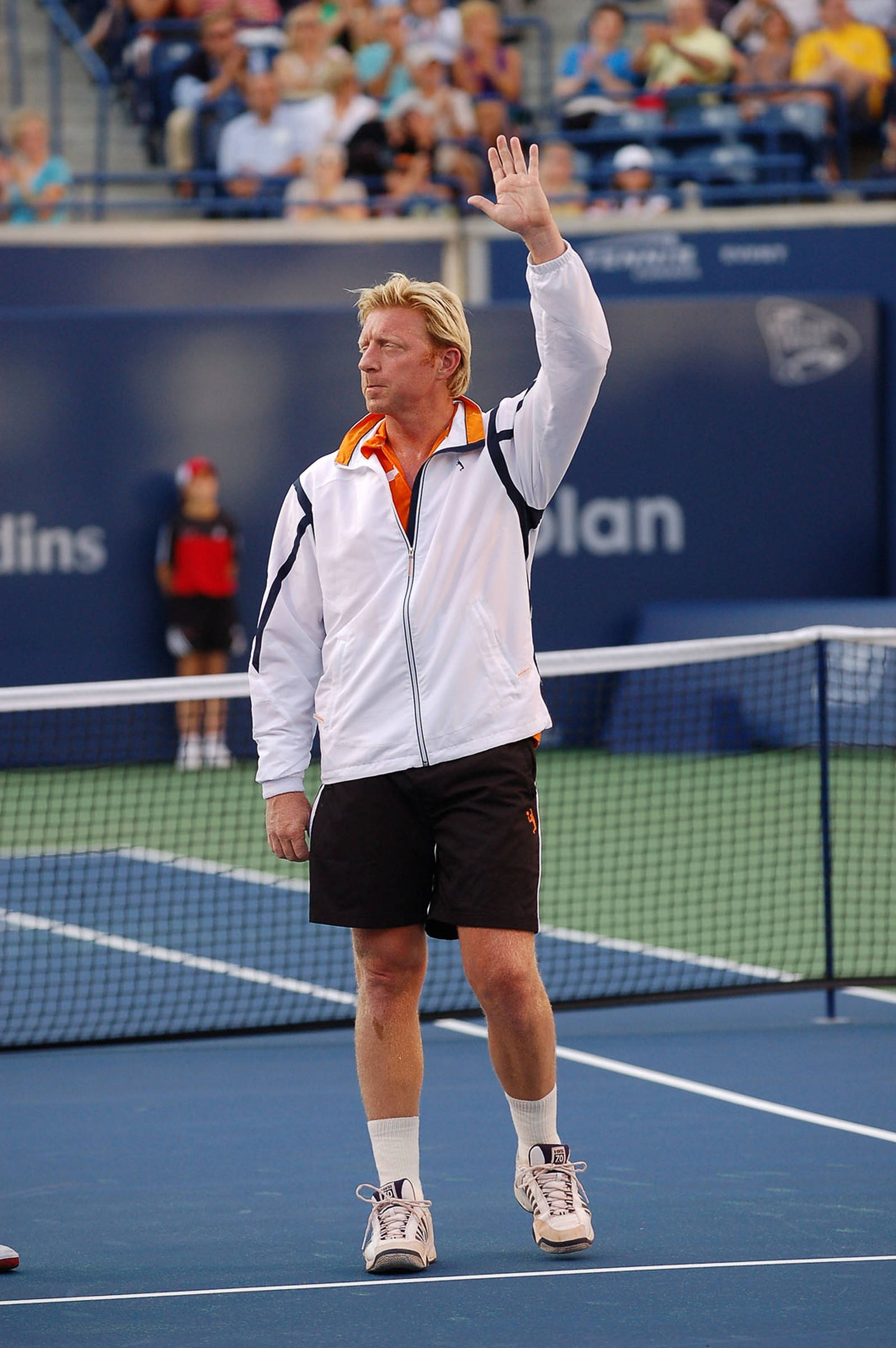 Boris Becker 桌布 壁紙 — 一位金髮網球選手身穿白色外套和黑色短褲，在明亮的日光下於藍色硬地球場向人群揮手。